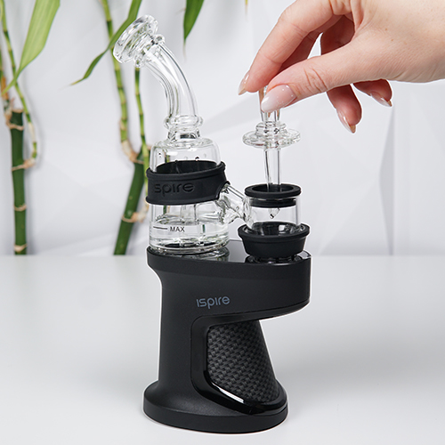 Ispire Daab Kit auf einem Tisch, während eine Frau einen Glas-Carb-Cap nahe der Heizkammer hält
