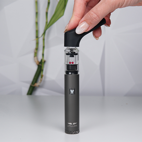 Ein Utillian 6 Dab Pen liegt auf einem Tisch, während eine Frau das ausziehbare Mundstück daran befestigt